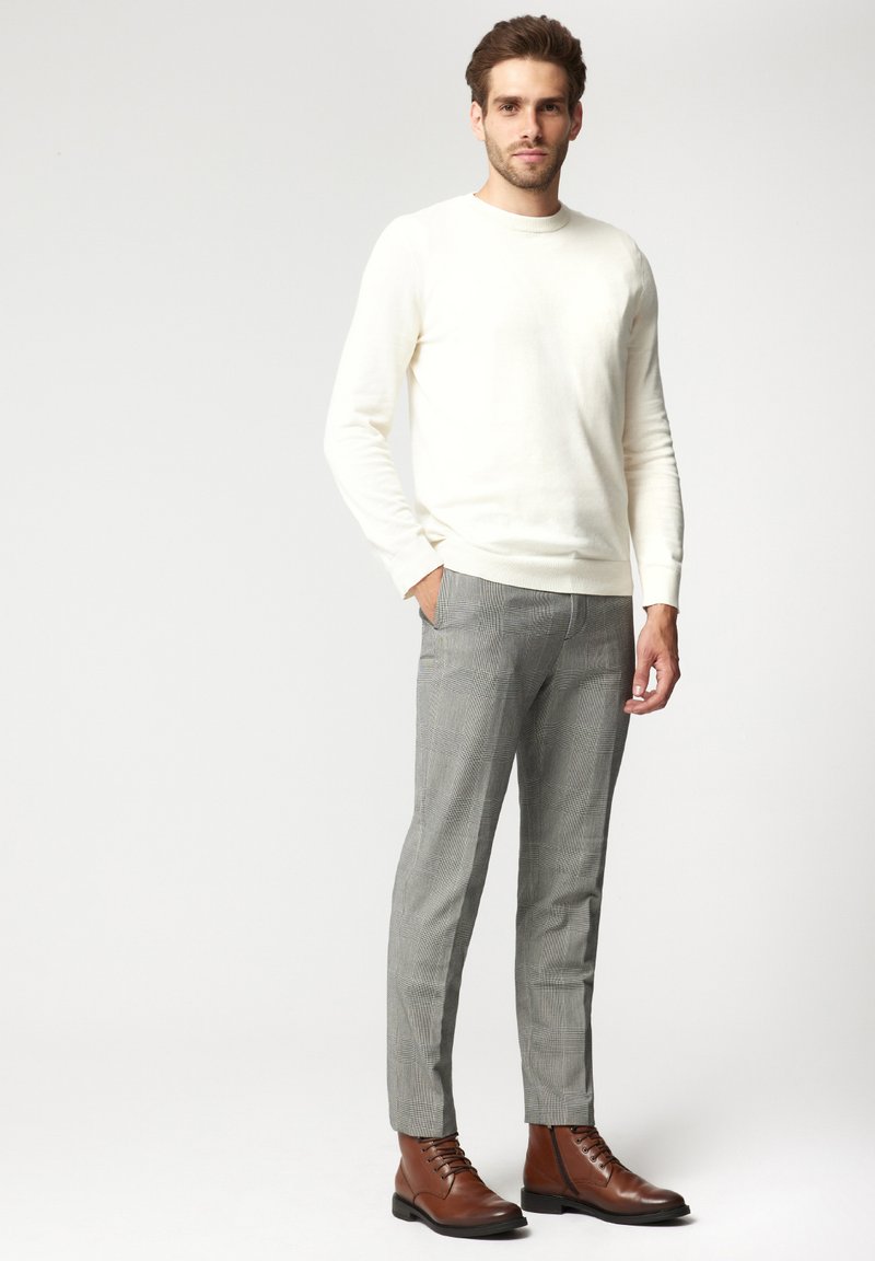 Kremowy sweter, szare spodnie w kratę i brązowe skórzane botki. Sweter ma okrągły dekolt, a spodnie są dopasowane i mają gładką teksturę.