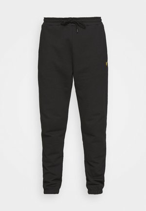 Pantalons de survêtement noirs avec une taille élastique à cordon, chevilles resserrées et un petit logo jaune. Fabriqués en tissu doux et texturé.