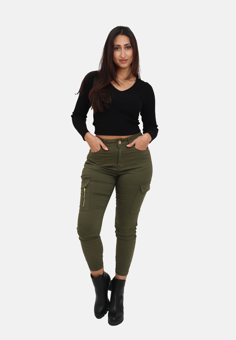 Un haut court noir à côtes associé à un pantalon cargo vert olive avec des poches zippées et une cheville fuselée. Le modèle porte des bottines noires.