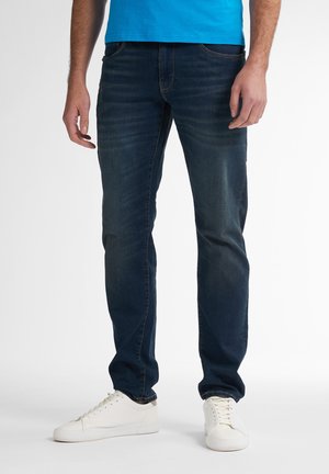 Dark blue denim jeans with a slim fit, five-pocket design, subtle fading, and a smooth texture. Paired with white sneakers.