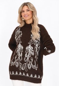 Pulover tricotat maro cu broderie florală albă, guler înalt, mâneci ample și modele decorative la margine. Textură moale, design casual.