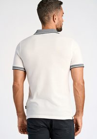 Vit kortärmad polo med mörkgrå krage och manschetter som har ett randigt mönster. Tillverkad av mjukt, texturerat tyg; figursydd design.