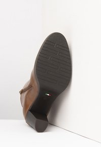 Brown leather ankle boot with a textured rubber sole, low block heel, and side zipper detail. Made in Italy, showcasing a smooth finish.