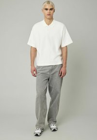 Polo-shirt blanc à manches courtes avec un col, associé à un jean gris clair à coupe décontractée et des baskets noir et blanc. Design simple, sans motifs.