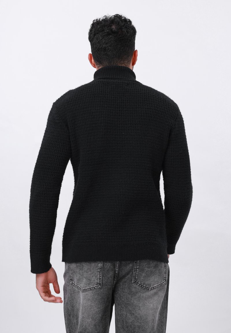 Maglione nera lavorato a maglia con colletto alto e tessuto texturizzato, abbinato a jeans grigi sbiaditi, mostrato da dietro su uno sfondo bianco.