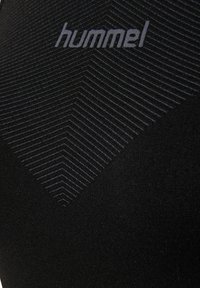 Sort stof med diagonale hvide linjer, der danner en V-form, og ordet "hummel" centreret nær toppen.