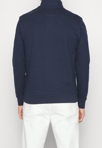 Felpa a maniche lunghe blu navy con colletto alto e polsini a coste. Realizzata in materiale morbido, con una texture liscia e senza motivi visibili.