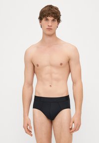 Juodos trumpikės su minkštu elastingu juosmeniu, kuriame išraižytas logotipas. Lygaus audinio, prigludusiame stiliuje, minimalus siūlių skaičius ir klasikinė forma.