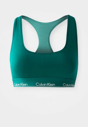 Teal sport-bh med rund hals og racerback-design. Har et bredt elastisk bånd med "Calvin Klein"-merke i hvitt. Glatt tekstilstruktur.