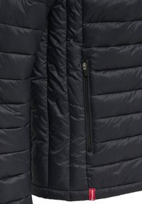 Marineblå pufjakke med quiltet tekstur, har en lynlåslomme og et lille rødt mærke ved kanten. Letvægts- og isoleret design.