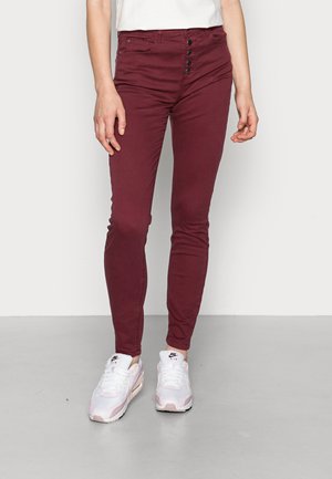 Bordeauxfärgade skinny jeans med framsida knappar, mjukt denimmaterial och medelhög midja, tillsammans med vita och rosa sneakers.