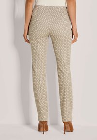 Beige aansluitende broek met een geometrisch patroon in lichtbruin en crème. Glad textuur en tapered fit, gecombineerd met bruine stiletto-hakken.