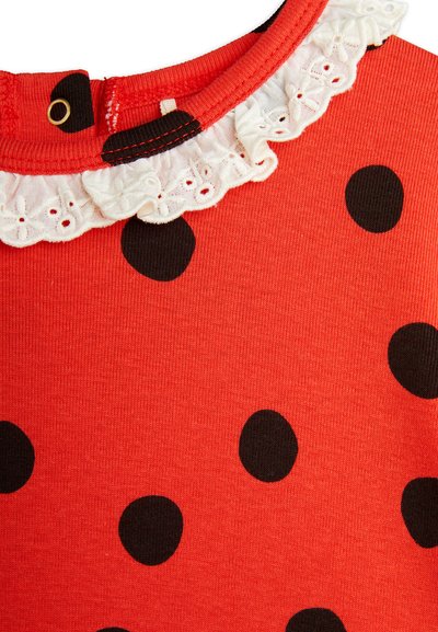 Haut en coton rouge à pois noirs, doté d'une bordure en dentelle blanche autour du cou. Le tissu texturé côtelé offre de l'élasticité.