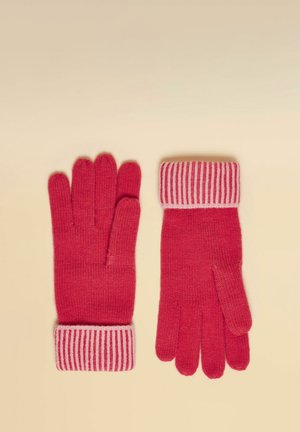 Para czerwonych dzianinowych rękawiczek z różowo-czerwonymi paskowanymi mankietami, rozłożonych na płasko na beżowej powierzchni, pokazujących przód i tył.