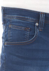 Denim jeans featuring dark blue fabric, contrasting orange stitching, a front pocket, and a metal button closure. Smooth texture.