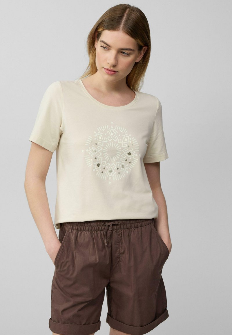 T-shirt en coton beige à manches courtes et col rond, doté d'un imprimé géométrique blanc au centre. Assorti à un short marron.