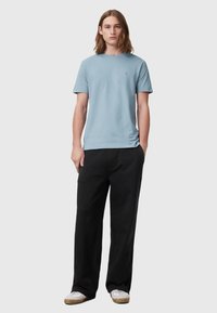 T-shirt di cotone blu chiaro con collo rotondo, abbinata a pantaloni neri larghi. La parte superiore presenta maniche corte e un logo discreto sul petto.