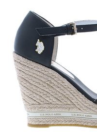 Sandalo con tacco a cuneo in pelle sintetica nera, con piattaforma in corda di juta, cinturino alla caviglia regolabile e un accento in oro con il logo vicino al tallone.