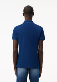 Polo shirt blu scuro in tessuto texturizzato, a maniche corte e con colletto classico, abbinato a jeans azzurri chiari.