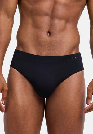 Torace maschile muscoloso che indossa slip neri stile brief con piccolo logo "FALKE" sulla fascia in vita, su sfondo semplice.