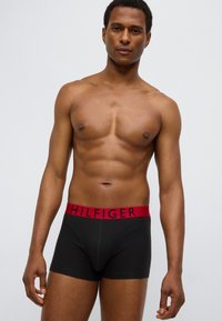 Μαύρα βαμβακερά μποξεράκια με  κόκκινη ζώνη μέσης που φέρει τη λέξη "HILFIGER" με μαύρα γράμματα. Η εφαρμογή είναι στενή, με ομαλή υφή.