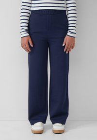 Marineblauwe wijde broek met een elastische tailleband, gemaakt van zacht materiaal, gecombineerd met witte sneakers met een beige zool.