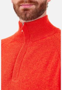 Roter Pullover mit Reißverschluss und hohem Kragen. Aus strukturiertem Strickstoff gefertigt, verfügt er über ein halb geöffnetes Reißverschluss-Design und gerippte Akzente am Kragen.