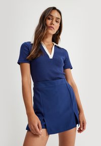 Polo de color azul marino con canalé y cuello blanco, combinado con una falda corta ajustada con abertura lateral, confeccionada en tejido suave, diseñada para un aspecto a medida.