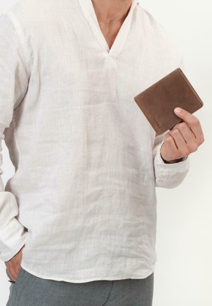 Bruine leren portemonnee vastgehouden in de hand, met een gladde textuur en subtiele stiksels, op de achtergrond van een licht linnen overhemd.