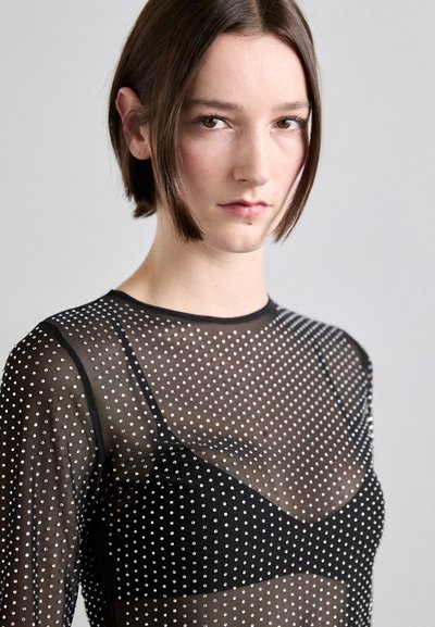Schwarzes, transparentes Langarmoberteil mit silbernen Punkten. Verfügt über einen runden Ausschnitt und eine figurbetonte Silhouette, kombiniert mit einem schwarzen Bralette darunter.
