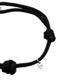 Schwarze geflochtene Schnur-Halskette mit doppelten Knotendetails und einem kleinen silbernen Etikett mit einem Logo. Strukturierte Oberfläche verleiht Tiefe.