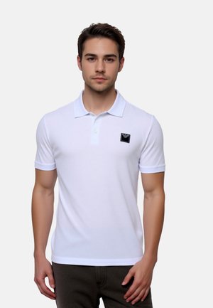 Weißes Poloshirt aus Baumwolle mit einem schwarzen Logo-Patch auf der Brust, kurzen Ärmeln und klassischem Kragen.