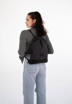 Drawstring backpack in dark gray fabric with a black bottom panel. Features adjustable straps and a small branded tag at the base.