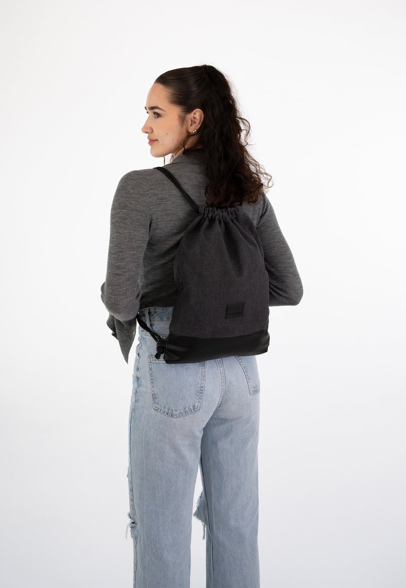 Reppu nyöri tummanharmaasta kankaasta, jossa on musta alaosa. Varustettu säädettävillä olkahihnoilla ja pienellä bränditunnuksella pohjassa.