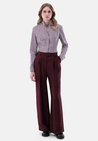 Camicia a righe bianca e bordeaux abbinata a pantaloni larghi bordeaux a vita alta. Scarpe nere completano l'outfit.