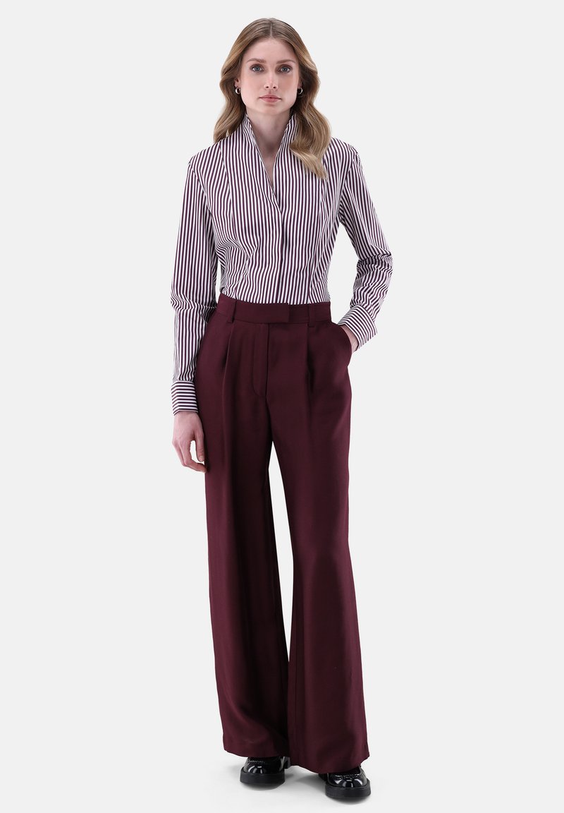Camicia a righe bianca e bordeaux abbinata a pantaloni larghi bordeaux a vita alta. Scarpe nere completano l'outfit.