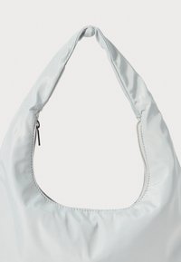 Vit satinaxelväska med ett böjt, mjukt handtag och en dragkedjestängning, med subtil sömnad och en slät yta.