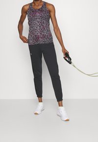 Svart och rosa mönstrad tanktop, parat med svarta joggare och vita sneakers. Outfitten har en sportig design med en kroppsnära passform.