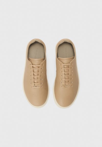 Kerged nahast tennikeid, mille pind on sile, ümmarguse varbaga ja paeltele kinnitatud esiosaga. Minimalistlik disain koos valge tallaga.