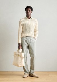 Beige knitted sweater, light green collared shirt, gray linen pants, beige shoes, holding a canvas bag. Smooth textures, relaxed fit.