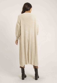 Cardigan long en tricot léger beige avec une coupe ample, des épaules tombantes et des poignets côtelés. Présente un motif texturé.