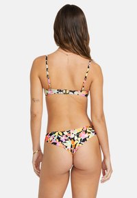 Květinové bikini se černým základem a barevnými vzory listů, tenkými nastavitelnými ramínky a sponou na zádech.