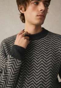 Strickpullover mit einem Chevron-Muster in Dunkelgrau und Hellgrau, Rundhalsausschnitt und gerippten Bündchen. Weiches, strukturiertes Material.