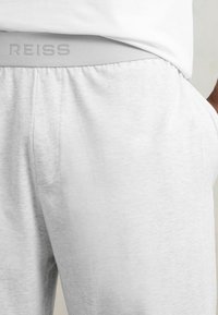 Svetlo šedé jogger nohavice s jemnou textúrou, so zúženým elastickým pásom s embosovaným nápisom "REISS" a bočnými vreckami.