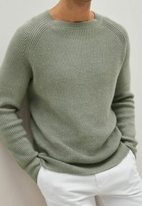 Lichtgroene ribgebreide trui met een ronde hals en lange mouwen, met een relaxte pasvorm en een gestructureerde stof. Gecombineerd met witte pantalons.