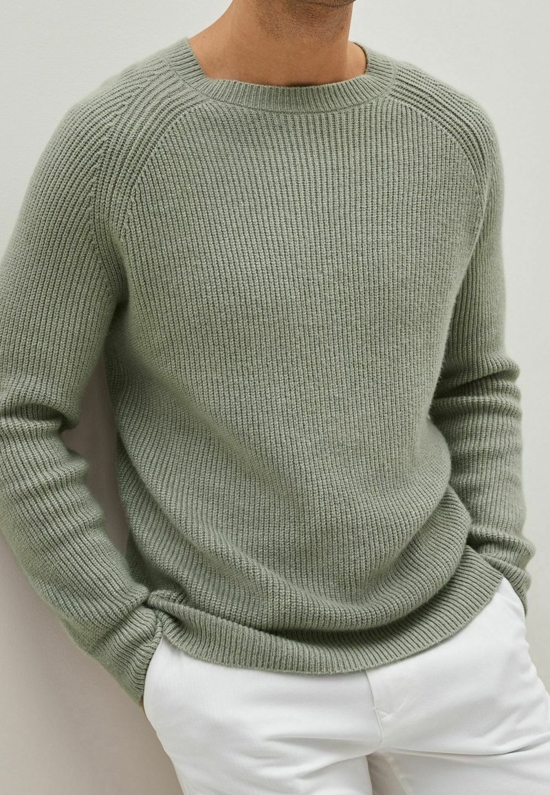 Lichtgroene ribgebreide trui met een ronde hals en lange mouwen, met een relaxte pasvorm en een gestructureerde stof. Gecombineerd met witte pantalons.