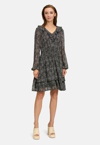Zwart-witte jurk met polka dots, ruffles bij de halslijn, lange doorschijnende mouwen, gelaagde rok en elastische taille. Draag het met lichtgekleurde platform schoenen.