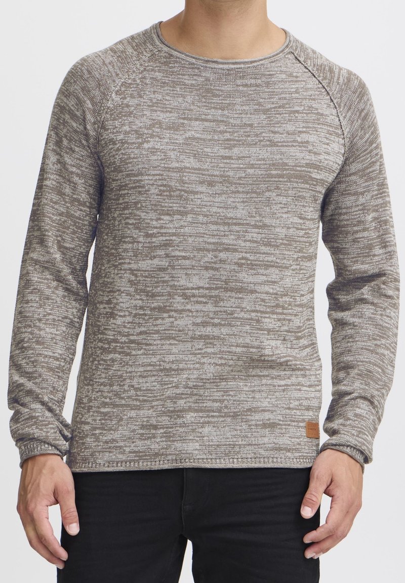 Pull en mailles marbrées brunes avec un col rond, des manches longues, des poignets côtelés et une petite étiquette en cuir au bas. Texture douce.