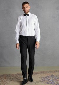 Cămașă albă cu guler cu papion, asortată cu pantaloni negri adaptați și cizme negre lucioase până la glezne. Material neted, siluetă croită.