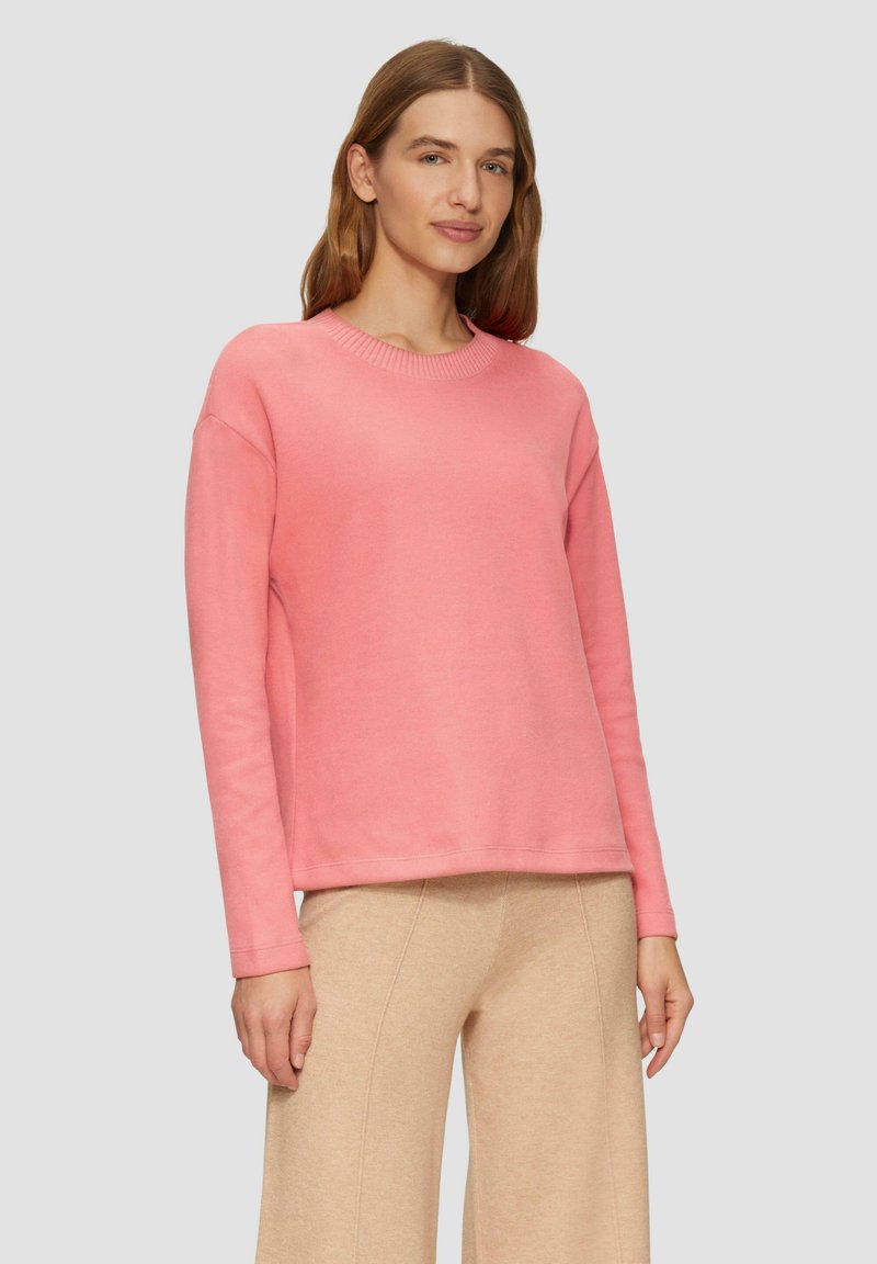 Roze trui met een ronde halslijn en lange mouwen, gemaakt van een zachte stof. Het heeft een ontspannen pasvorm en ribbels aan de mouwen.